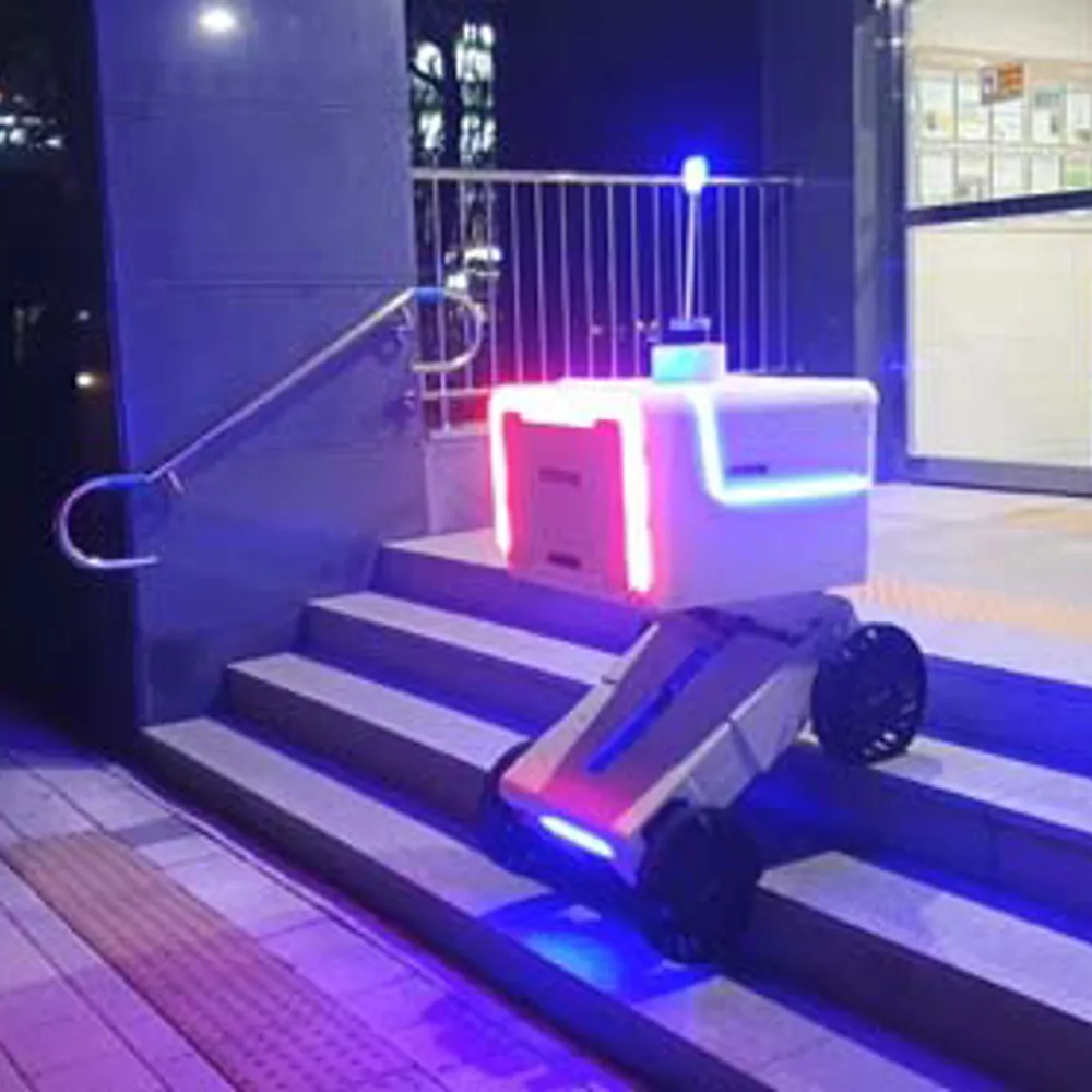 ALT Text: A delivery Robot going outside down a small flight of stairs on wheels with bright lights around the robot